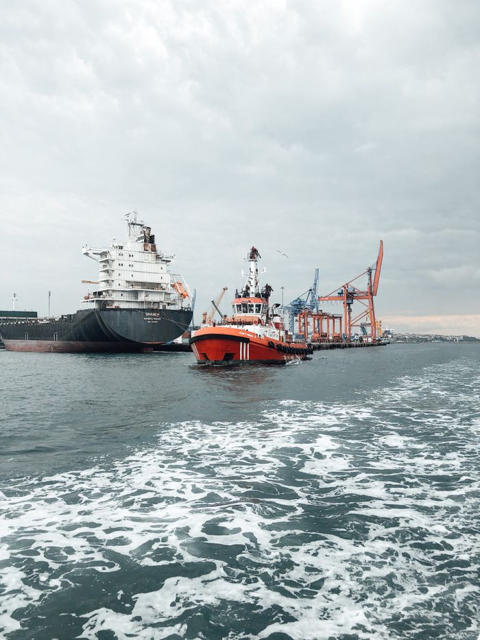 A tugboat guides a cargo ship at a bustling port, emphasizing maritime transport.